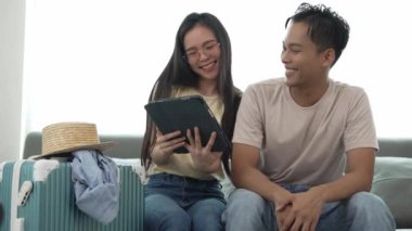 Asyalı çift yurt dışına gitmek için eşyalarını topluyor. Yatak odasında, kadın ve erkek, oturma odasında, bavulların yanında, özel eşyaları tatile gidiyor.