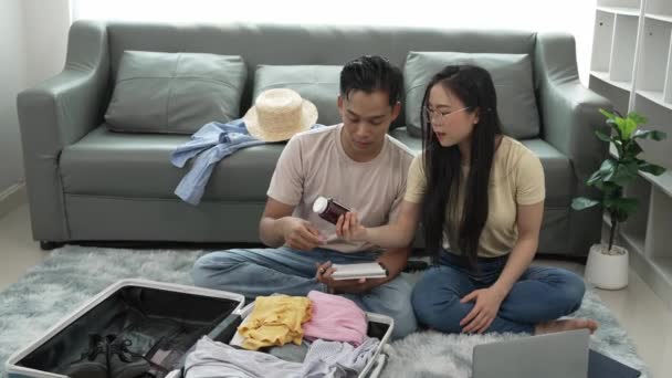 アジアのカップルは ベッドルームで一緒に海外旅行のための服を梱包 スーツケースの近くのリビングルームの床に座っている男女 休暇中に持ち物と — ストック動画