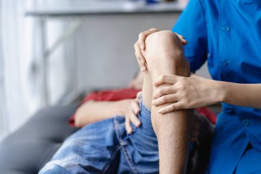 Fizik tedavi konsepti erkek bir hastanın yaralı dizini klinikte tedavi eder. Omuz eklemlerini tedavi eden bir hastanın elini tutan bir fizyoterapist, hastaya omuz kası ağrısı hakkında danışır..