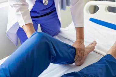 Fizik tedavi konsepti erkek bir hastanın yaralı dizini klinikte tedavi eder. Omuz eklemlerini tedavi eden bir hastanın elini tutan bir fizyoterapist, hastaya omuz kası ağrısı hakkında danışır..