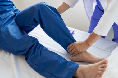 Fizik tedavi konsepti erkek bir hastanın yaralı dizini klinikte tedavi eder. Omuz eklemlerini tedavi eden bir hastanın elini tutan bir fizyoterapist, hastaya omuz kası ağrısı hakkında danışır..