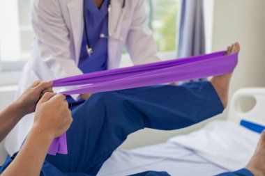 Fizik tedavi konsepti erkek bir hastanın yaralı dizini klinikte tedavi eder. Omuz eklemlerini tedavi eden bir hastanın elini tutan bir fizyoterapist, hastaya omuz kası ağrısı hakkında danışır..