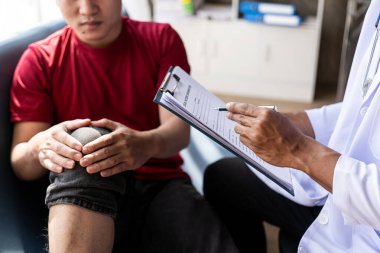 Genç adam diz eklem ağrısı hakkında konuşuyor, doktor. Doktorun muayenehanesinde ilaçların ve yan etkilerin nasıl alınacağını. Adam dikkatle doktorun tavsiyesini dinledi..