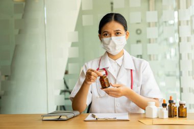 Asyalı kadın doktor, elinde ilaç şişesi, teletıp konsepti ve sağlık hizmeti ile hastasına ilaç prosedürünü video üzerinden açıklıyor.