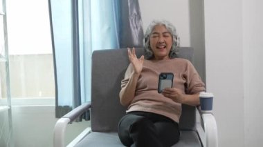 Kanepede oturan yaşlı kadın ya da Asyalı büyükanne internet üzerinden ödemek için cep telefonu kullanıyor, oyunlar oynuyor, film izliyor, müzik izliyor, sosyal medya evinde oturuyor..