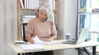 Gülümseyen orta yaşlı kadın çalışan bilgisayarla masada oturuyor, ofis hesapları yapıyor..