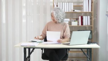 Gülümseyen orta yaşlı kadın çalışan bilgisayarla masada oturuyor, ofis hesapları yapıyor..