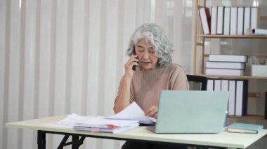 Gülümseyen orta yaşlı kadın çalışan bilgisayarla masada oturuyor, ofis hesapları yapıyor..