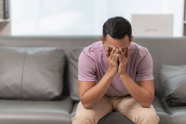 Baş ağrısı ya da migrenden muzdarip üzgün bir adam şakaklarına dokunuyor, kafasına masaj yapıyor, yüzünde acı dolu bir ifadeyle kanepede oturuyor. Zayıf ya da depresif hissediyorum.