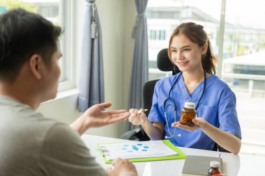 Genç Asyalı doktor iyi haberler veriyor ve klinikteki bir masada oturan erkek hastayla sonuçları ya da belirtileri tartışıyor..