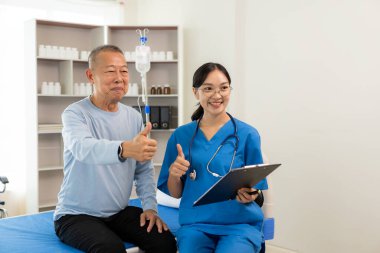 Güzel hemşire doktor, yaşlı bir erkek hastayı yatakta yatırıp desteklerken ve konuşurken mutlu hissediyor..