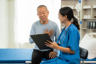 Güzel hemşire doktor, yaşlı bir erkek hastayı yatakta yatırıp desteklerken ve konuşurken mutlu hissediyor..