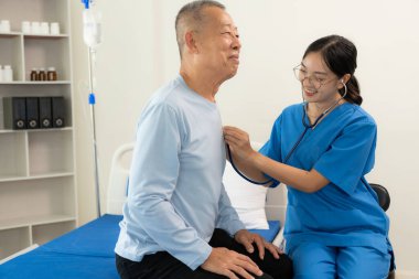 Güzel hemşire doktor, yaşlı bir erkek hastayı yatakta yatırıp desteklerken ve konuşurken mutlu hissediyor..