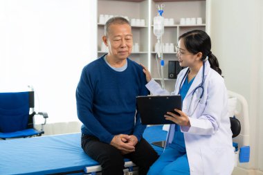 Güzel hemşire doktor, yaşlı bir erkek hastayı yatakta yatırıp desteklerken ve konuşurken mutlu hissediyor..