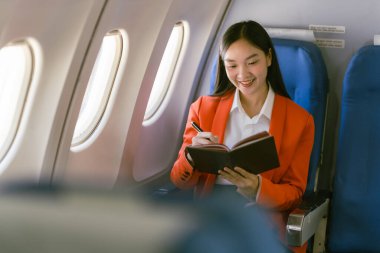 Genç Asyalı kadın gezgin pencerenin yanında oturuyor ve pencereden dışarı bakıyor. Elinde not defteri, yürüme konsepti var.