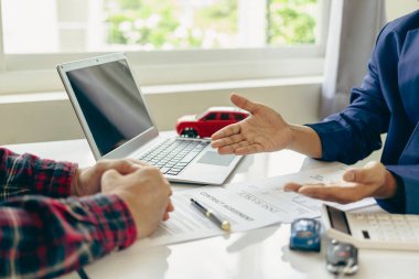 Küçük bir araba ve araba anahtarıyla masada oturan bir müşteriyi tanıtan bir satıcının yakın plan görüntüsü. Araba satıcısı ve yeni sahibi araba satmak ve kiralamak için kontrat yaptı..