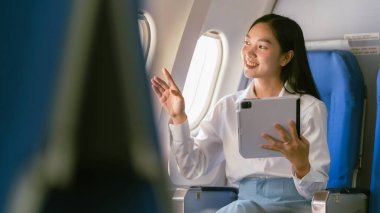 Uçuş, seyahat ve iş konsepti sırasında pencerede otururken tablet tutan Asyalı kadın