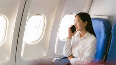 Uçakta otururken telefona bakan Asyalı bir kadın. Teknoloji kadın yolcuları cep telefonları, online uygulamalar ve seyahat sırasında uçak koltuklarında otururken internet kullanıyorlar..