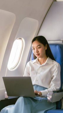 Uçakta dizüstü bilgisayar kullanan profesyonel bir Asyalı kadın uçuş konsepti sırasında birinci sınıfta uçağın penceresinin yanında oturuyordu.