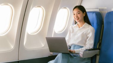 Uçakta dizüstü bilgisayar kullanan profesyonel bir Asyalı kadın uçuş konsepti sırasında birinci sınıfta uçağın penceresinin yanında oturuyordu.