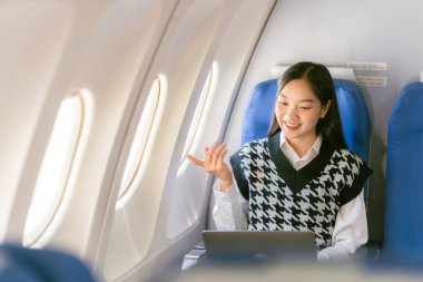 Uçakta dizüstü bilgisayar kullanan profesyonel bir Asyalı kadın uçuş konsepti sırasında birinci sınıfta uçağın penceresinin yanında oturuyordu.