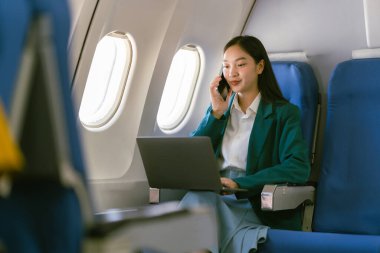 Uçakta dizüstü bilgisayar kullanan profesyonel bir Asyalı kadın uçuş konsepti sırasında birinci sınıfta uçağın penceresinin yanında oturuyordu.