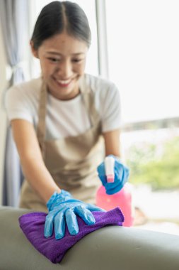 Genç ve güzel Asyalı kadın ev işi yapıyor ve evi temizliyor. Ev temizleme aletleriyle gülümsüyor.