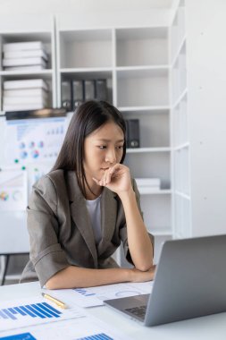 Asyalı iş kadını bir masanın arkasında oturmuş elinde borsa grafiği olan bir monitöre bakıyor. Büyük veri analizi modern iş ofisindeki ticarete yardımcı olur