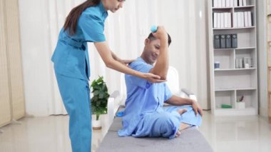 Bir hemşire, erkek bir hastaya hastanede fizik tedavi uygulamaya yardımcı olur. Asyalı erkek hasta, sağlık sigortası konseptinde tedavi görüyor