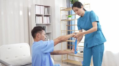 Bir hemşire, erkek bir hastaya hastanede fizik tedavi uygulamaya yardımcı olur. Asyalı erkek hasta, sağlık sigortası konseptinde tedavi görüyor