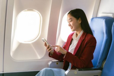 Genç Asyalı bir kadın uçakta oturuyor ve akıllı bir telefonla konuşuyor. Ekonomi sınıfında pencere kenarında otururken bir uçak uçuşu sırasında akıllı bir cep telefonu kullanıyor.