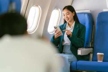 Genç Asyalı bir kadın uçakta oturuyor ve akıllı bir telefonla konuşuyor. Ekonomi sınıfında pencere kenarında otururken bir uçak uçuşu sırasında akıllı bir cep telefonu kullanıyor.