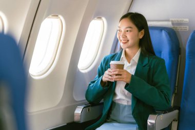 Uçakta oturan ve pencereden dışarı bakan Asyalı kadın, seyahat konsepti, turizm, iş