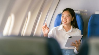 Asyalı kadın tabletten e-posta okuyor. Eğlence olsun diye online oyunlar oynuyor. Uçak koltuğunuzun birinci sınıf konforunun keyfini çıkartıyor..