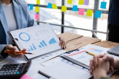 Bir iş sunumu ya da seminerinde konferans salonunda çalışan farklı uluslardan bir grup insan. Belgelerde mali rakamlar, grafikler, grafikler ve dizüstü bilgisayarın yakın çekimleri yer alıyor.