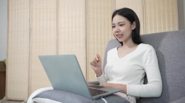 Kanepede dizüstü bilgisayar kullanan genç Asyalı bir kadın bilgisayarında internette sörf yapan arkadaşlar ve kız arkadaşlarla uzaktan konuşmak için bir e-posta yazın. ev kavramından çalışma