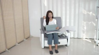 Asyalı kız kanepede oturup dizüstü bilgisayarla internette sörf yapıyor. ev kavramından çalışma