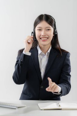 Kulaklık konseptini kullanarak iletişim merkezi ve müşteri hizmetleri, ofiste çalışan kulaklık takan güzel Asyalı kadın ve iş yerindeki müşterileri desteklemek için dizüstü bilgisayarı kullanarak sohbet etmek.