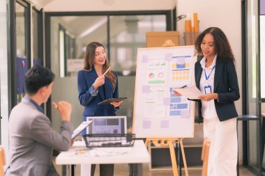 Asyalı başarılı iş adamlarından oluşan bir ekip takım toplantı dakikalarını ve ofis işbirliği fikirlerini sunuyor..