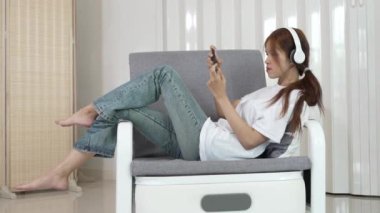 Cute Asian woman smiling happily, enjoying using smartphone, surfing the internet, social media, relaxing, technology in daily life in life.