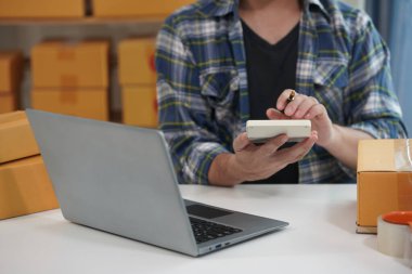 KOBİ işi. Bilgisayarla çalışan genç bir adam. Masasında karton kutular var. Teslimata hazır..