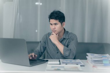 Asyalı işadamı mali durumu analiz etmek için fazla mesai yapıyor, bütçe üzerinde çalışıyor. Geceleri ofisteki hesap makinesiyle hesaplamak.