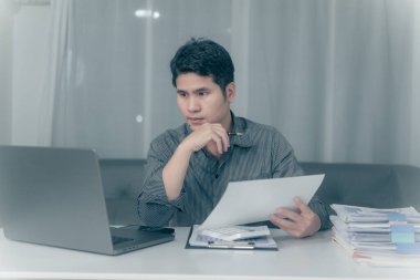 Asyalı işadamı mali durumu analiz etmek için fazla mesai yapıyor, bütçe üzerinde çalışıyor. Geceleri ofisteki hesap makinesiyle hesaplamak.