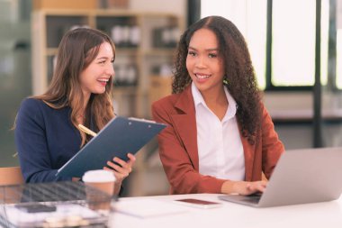 İki genç iş kadını laptoplarda çalışırken paneller hakkında konuşuyor, belgeler okuyor ve yeni bir projeyi tartışırken notlar yazıyorlar..