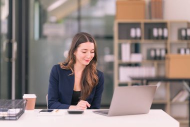 Kadın muhasebeci hesap makinesi kullanır ve iş verilerini hesaplamak için kalem tutar. İş kadını dizüstü bilgisayara bakar, harcamaları hesaplar, vergileri internetten öder, finansal dökümanlar.