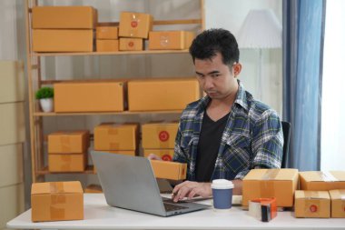 Genç Asyalı adam müşteriler için paket paketliyor. Elektronik ticaret, online alışveriş, KME iş konsepti. Bir adam bir paket kutusu tutuyor ve onu bir müşteriye göndermeye hazırlanıyor..