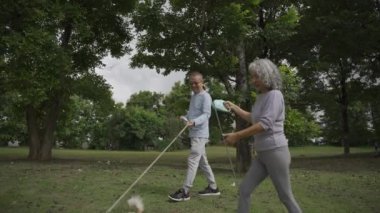 Parkta köpek gezdirme ve egzersiz yapan Asyalı yaşlı çift VDO Siow Hareketi