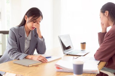 Asyalı kadın iki elini alnına bastırıyor. Stresli hissediyor. Belgeler ve dizüstü bilgisayarla kötü finansal işlerden endişe ediyor.