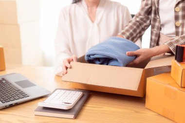 KOBİ iş konsepti: Genç bir girişimci çevrimiçi ürünleri satmak için kutularca ürün göndermeye hazırlanıyor ve bunları müşterilere göndermeye hazırlanıyor. Ev işlerinde internetten bir şeyler satmak