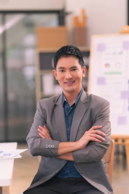 Genç Asyalı işadamı, bilgisayarla çalışırken gülümsüyor ve iş hayatında başarılı olma kavramına sahip.